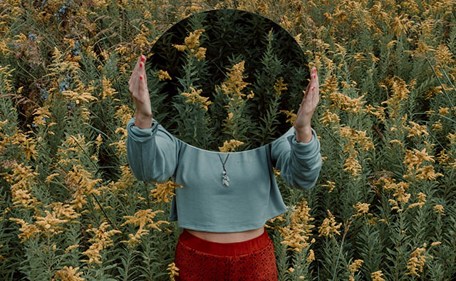 femme tenant un minoir devant elle dans un champs de plantes vertes et jaunes